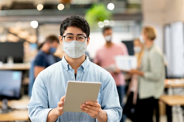 Asian man working online at a creative office and wearing a facemask