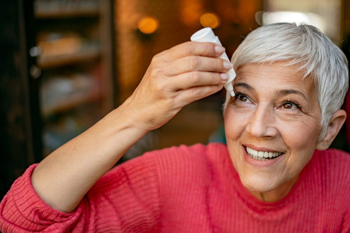 Photo of senior woman putting eye drop, closeup view of elderly person using bottle of eyedrops in her eyes. Sick old woman suffering from irritated eye, optical symptoms. Health concept. Concept of eye treatment, vision improvement, poor eyesight